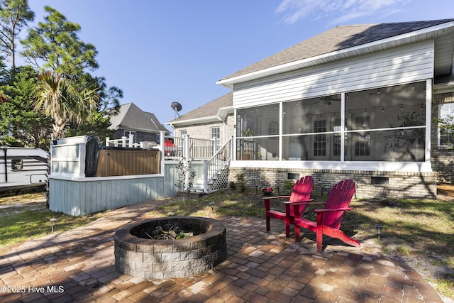 exterior space featuring roof with shingles, a sunroom, brick siding, a patio, and a fire pit