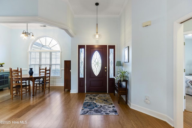 entryway featuring baseboards, ornamental molding, wood finished floors, and a notable chandelier