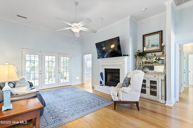 living room with a brick fireplace, a ceiling fan, ornamental molding, and light wood-type flooring