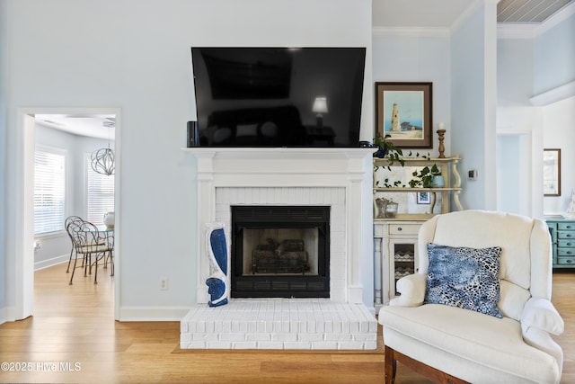 interior space featuring a brick fireplace, baseboards, ornamental molding, and wood finished floors