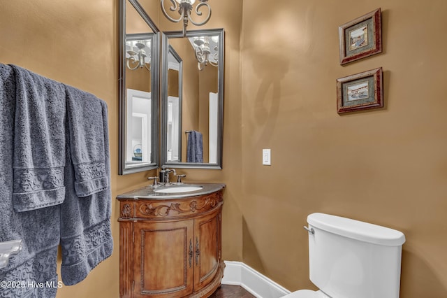 half bathroom with baseboards, a notable chandelier, toilet, and vanity