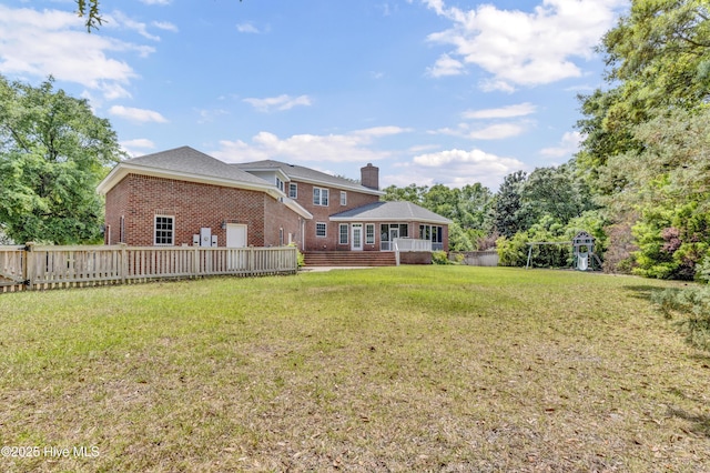 rear view of house with a chimney, a deck, brick siding, a fenced backyard, and a yard