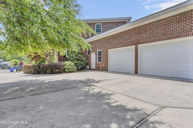 view of home's exterior with an attached garage, concrete driveway, and brick siding