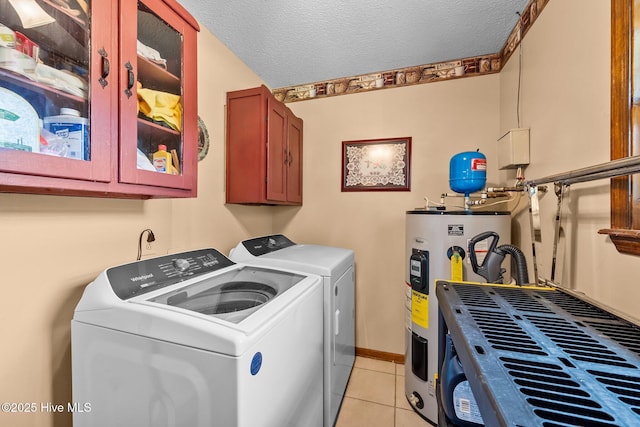clothes washing area featuring electric water heater, light tile patterned floors, washer and dryer, cabinet space, and a textured ceiling