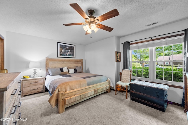 bedroom featuring a textured ceiling, visible vents, ceiling fan, and light carpet