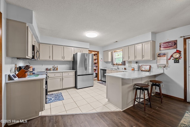 kitchen with stainless steel appliances, a peninsula, a textured ceiling, and light countertops
