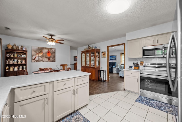 kitchen with stainless steel appliances, light tile patterned flooring, ceiling fan, light countertops, and a textured ceiling