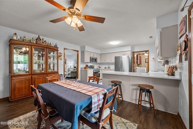 dining space featuring dark wood-style flooring, ceiling fan, washer / dryer, baseboards, and a textured ceiling