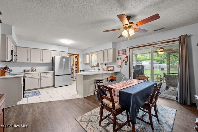 dining room featuring a textured ceiling, visible vents, a healthy amount of sunlight, light wood-style floors, and a ceiling fan