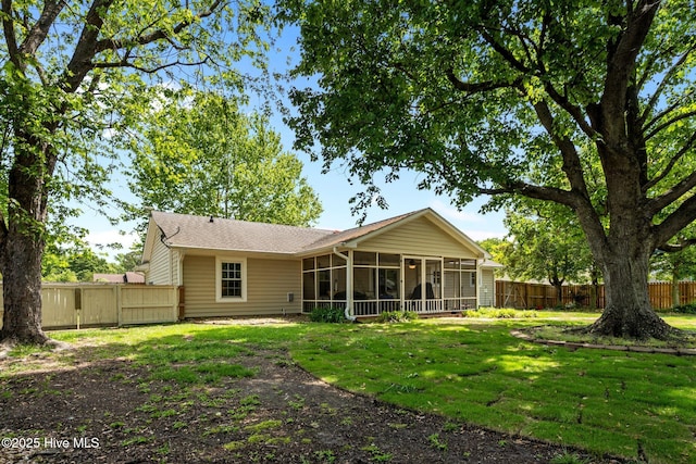 rear view of house featuring a lawn, a fenced backyard, and a sunroom