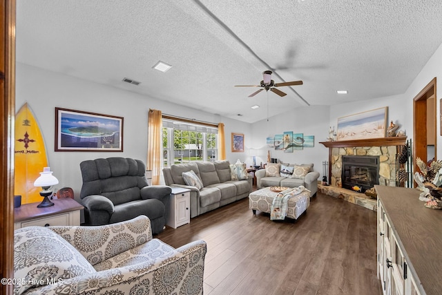living room with ceiling fan, a stone fireplace, dark wood-style flooring, visible vents, and a textured ceiling