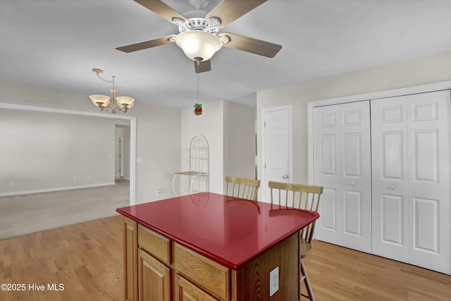 kitchen with a kitchen breakfast bar, a kitchen island, light wood-type flooring, ceiling fan with notable chandelier, and open floor plan