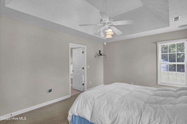 carpeted bedroom with connected bathroom, ceiling fan, a raised ceiling, baseboards, and visible vents