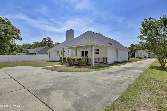 exterior space with fence, covered porch, roof with shingles, a chimney, and a lawn