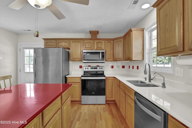 kitchen with appliances with stainless steel finishes, a sink, light wood finished floors, a wealth of natural light, and visible vents