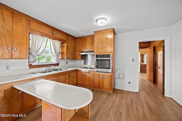 kitchen with a sink, light countertops, stainless steel oven, brown cabinetry, and under cabinet range hood