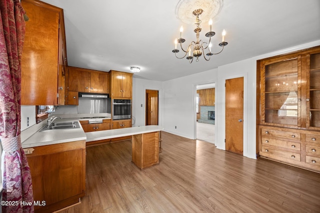 kitchen with oven, a notable chandelier, a sink, brown cabinetry, and a center island