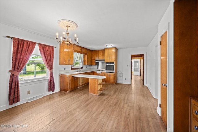 kitchen featuring oven, light countertops, a chandelier, brown cabinetry, and visible vents