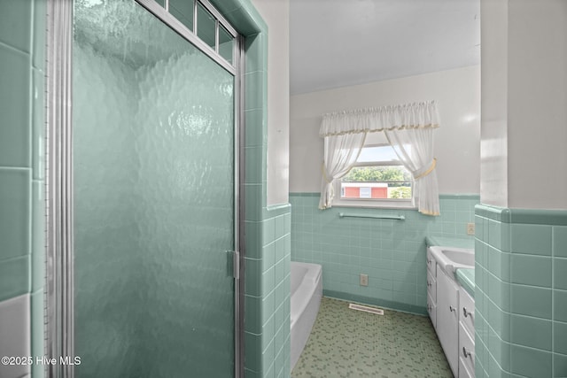 bathroom with a bath, wainscoting, a stall shower, and tile walls