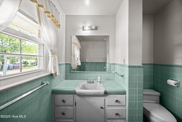 bathroom featuring vanity, tile walls, wainscoting, and toilet