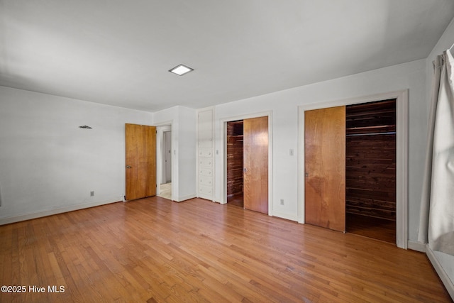 unfurnished bedroom featuring baseboards, multiple closets, and light wood-type flooring