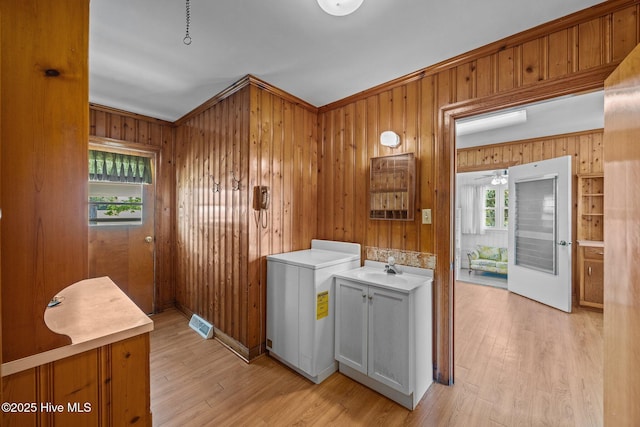 laundry room featuring a sink, ornamental molding, wood walls, and light wood-style flooring