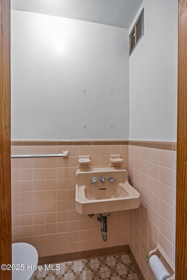 half bath with toilet, tile walls, wainscoting, and visible vents