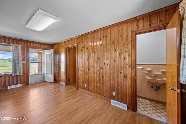 empty room with visible vents, wood walls, wood finished floors, and tile walls