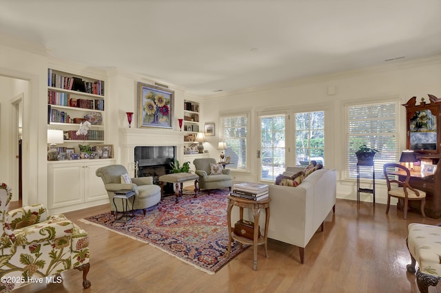 7102 Saybrook Dr, Wilmington, NC 28405 - living room featuring a tile fireplace, crown molding, built in shelves, and light wood-style flooring