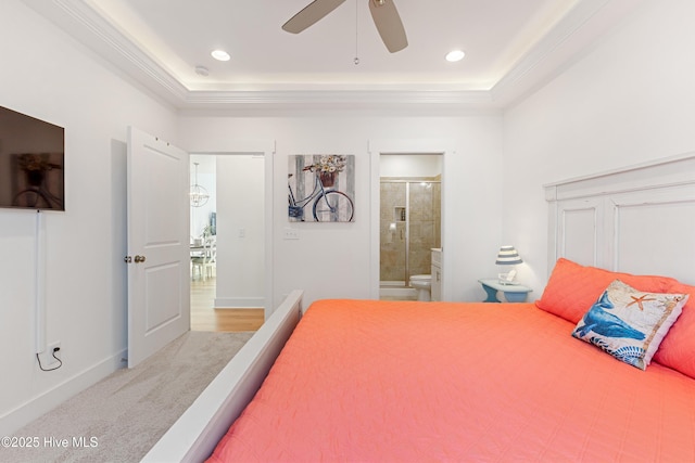 carpeted bedroom with baseboards, ornamental molding, a tray ceiling, and ensuite bath