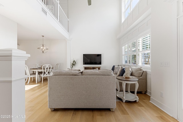 living area featuring light wood-style floors, visible vents, a healthy amount of sunlight, and a towering ceiling