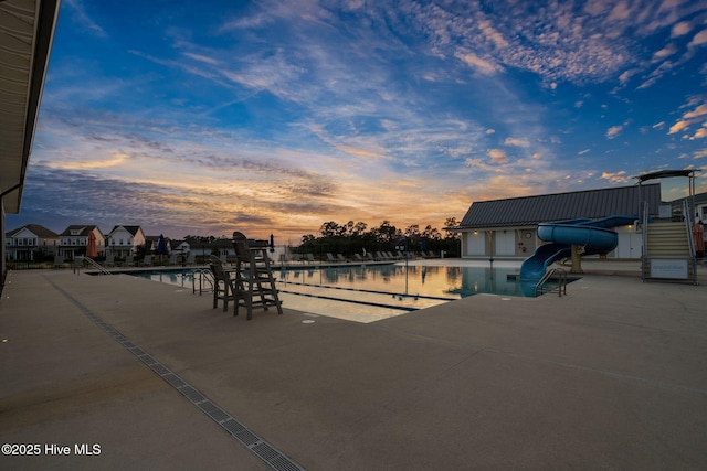 pool at dusk with a patio, a community pool, and a water slide
