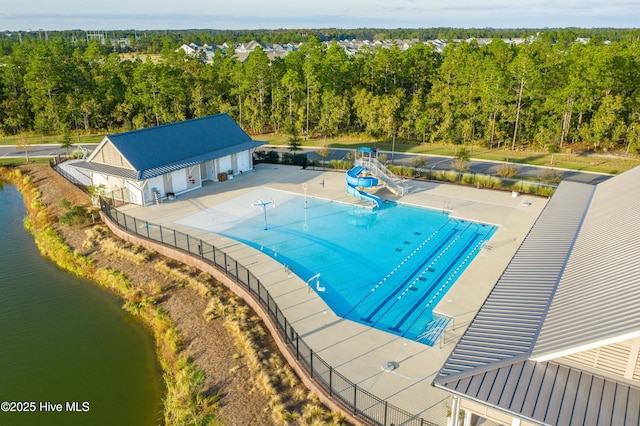 pool featuring fence, a patio, a water view, a water slide, and a wooded view