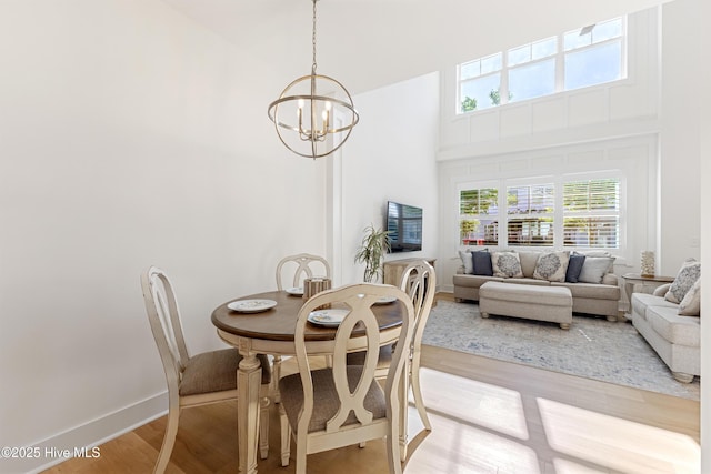 dining area featuring light wood-type flooring, baseboards, a towering ceiling, and a chandelier