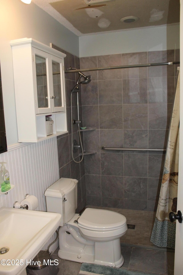 bathroom with a sink, a wainscoted wall, a tile shower, and toilet