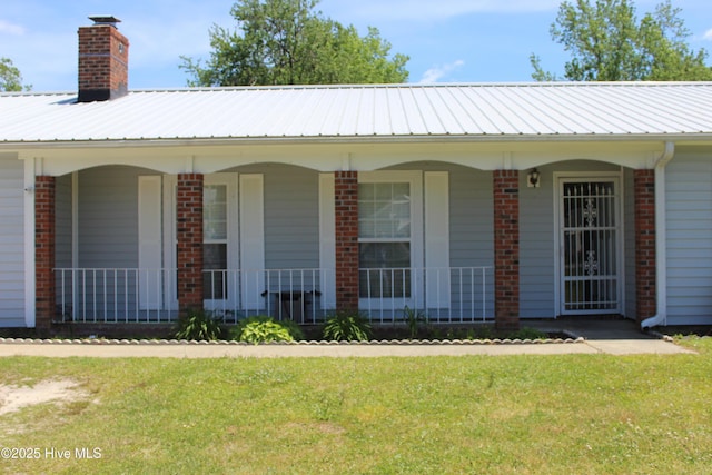 view of front of home featuring brick siding, covered porch, a chimney, and metal roof