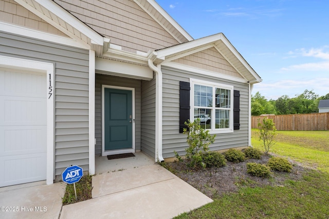 entrance to property featuring a lawn, an attached garage, and fence