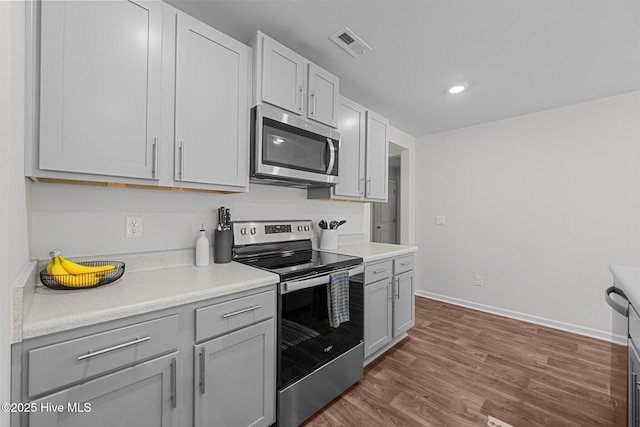 kitchen featuring visible vents, stainless steel appliances, light countertops, dark wood-style floors, and baseboards