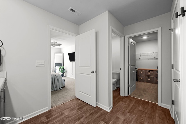 hall featuring dark wood-type flooring, visible vents, and baseboards