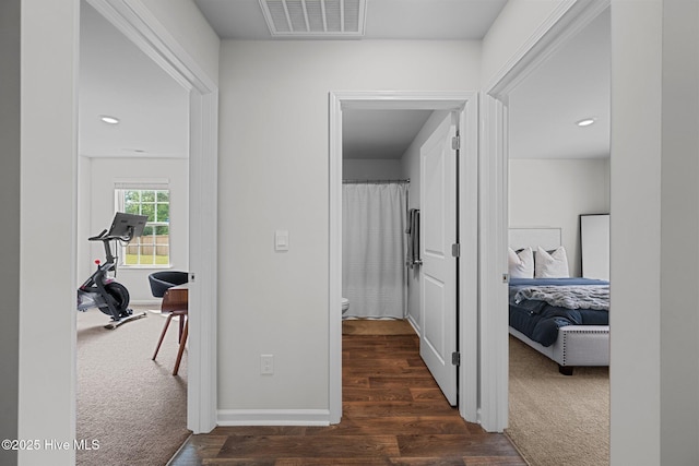 hallway featuring dark carpet, dark wood-type flooring, visible vents, and baseboards