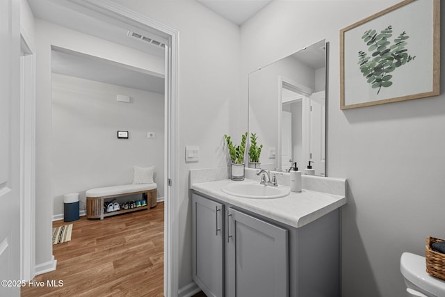 half bath featuring toilet, wood finished floors, vanity, and visible vents