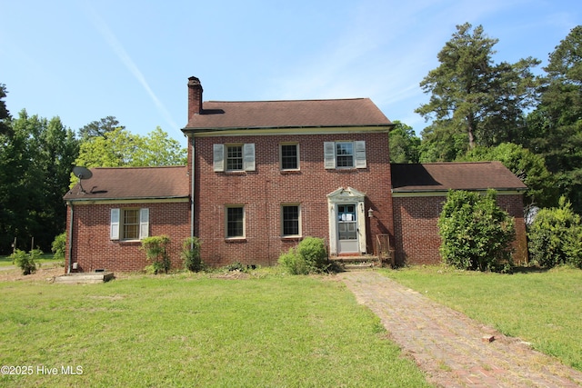 colonial inspired home with a chimney, brick siding, and a front yard