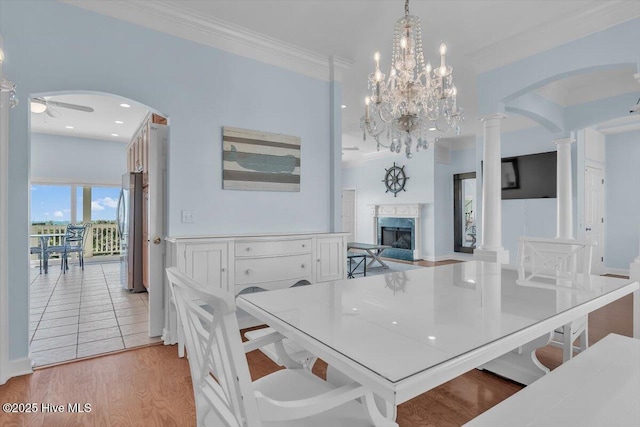 3720 Island Dr, North Topsail Beach, NC 28460 - dining room featuring a fireplace, arched walkways, light wood-style flooring, ceiling fan with notable chandelier, and ornate columns