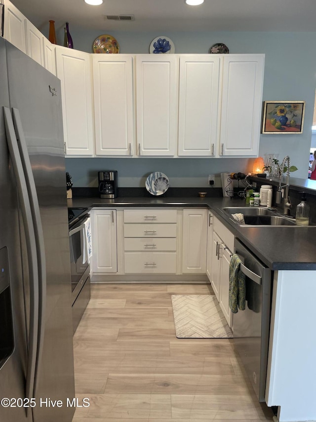kitchen with visible vents, dark countertops, white cabinets, light wood finished floors, and stainless steel appliances