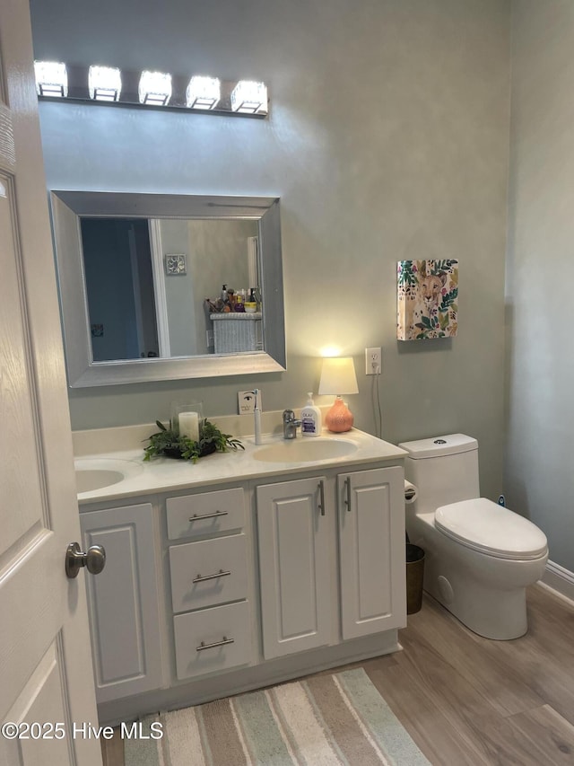 bathroom featuring double vanity, toilet, a sink, and wood finished floors