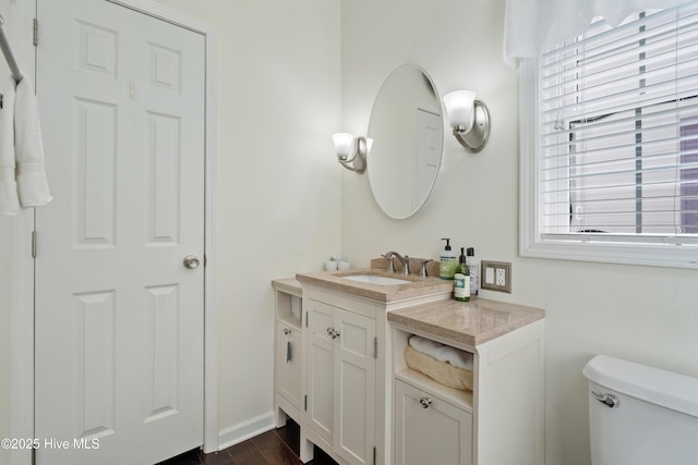 half bath with wood finished floors, toilet, and vanity