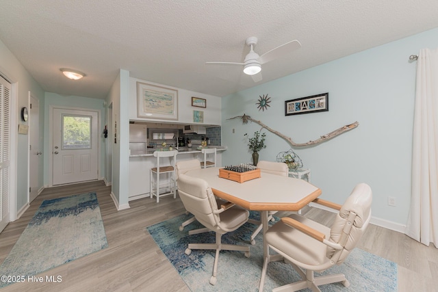 dining area featuring baseboards, a ceiling fan, light wood-type flooring, and a textured ceiling