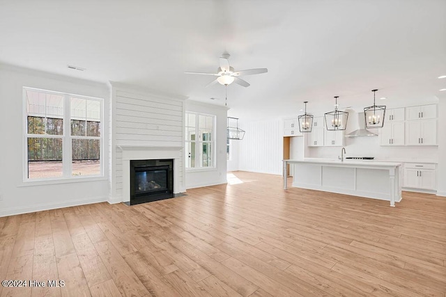 unfurnished living room with a large fireplace, light wood-style flooring, ceiling fan with notable chandelier, baseboards, and visible vents