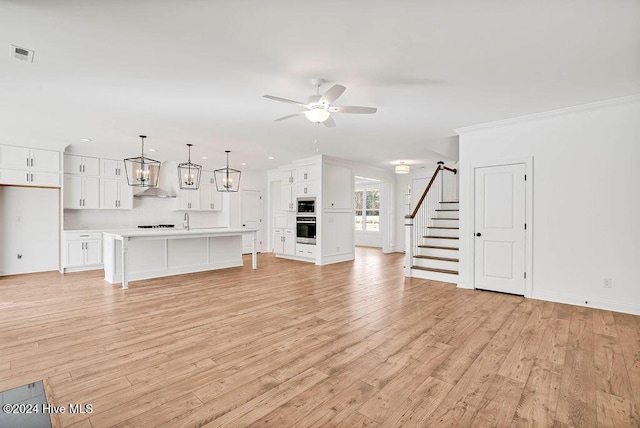 unfurnished living room with visible vents, light wood-style flooring, stairs, and ceiling fan