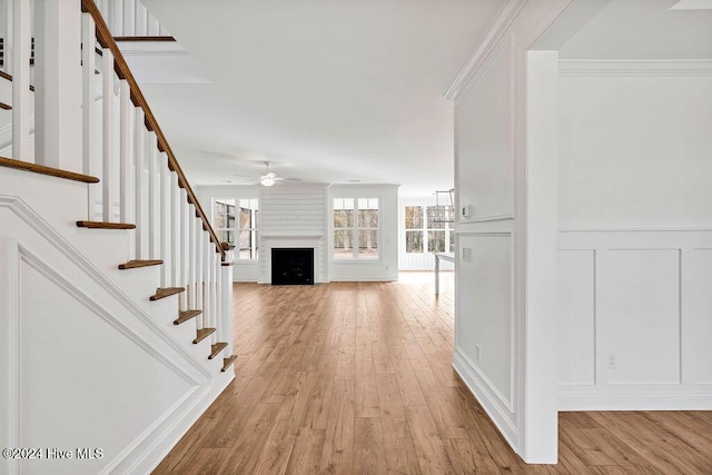 interior space featuring light wood-style floors, a decorative wall, a large fireplace, stairs, and a ceiling fan